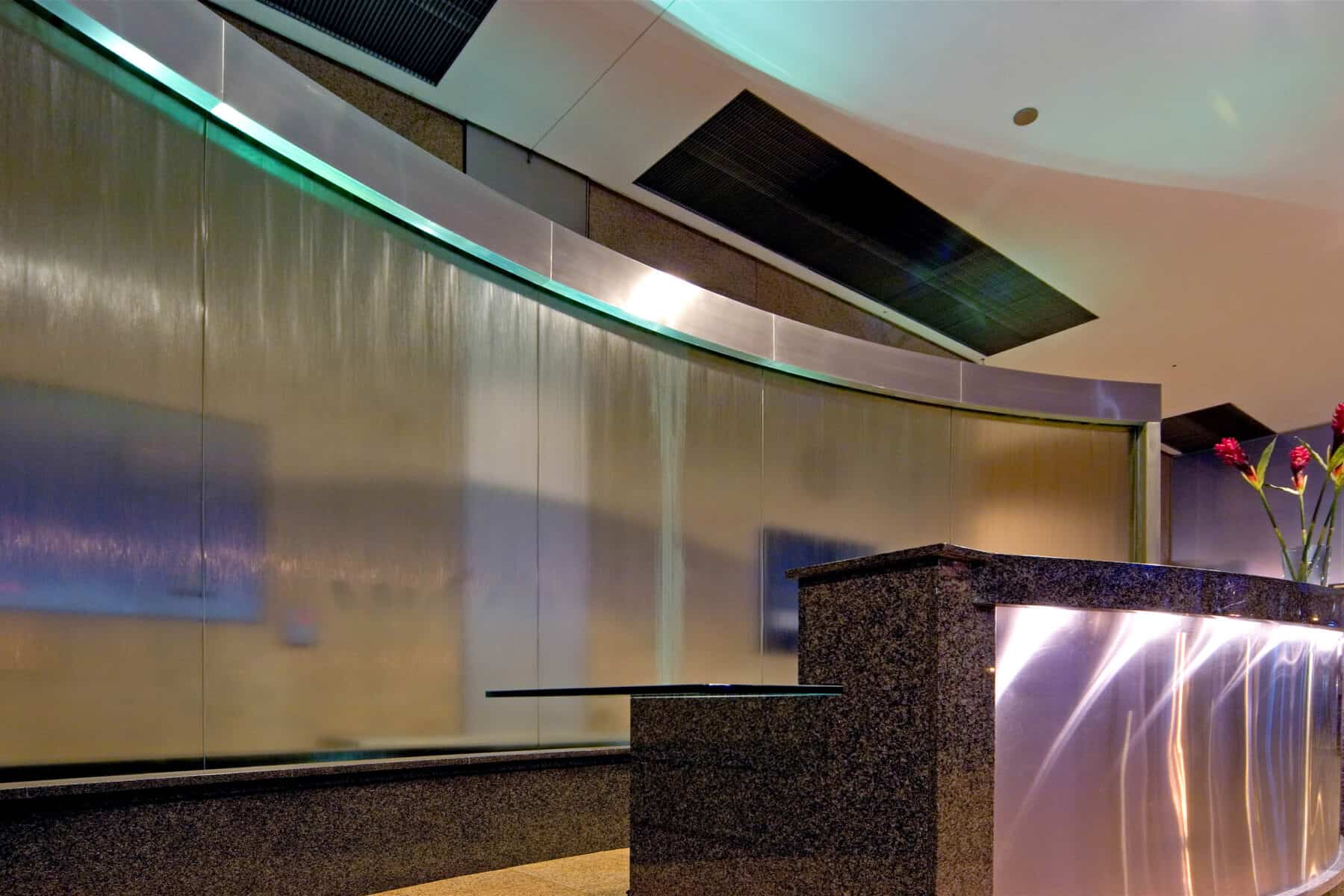 Custom Curved Glass Water Feature Behind Stone and Metal Reception Desk by Commercial Builder & General Contractor Structural Enterprises