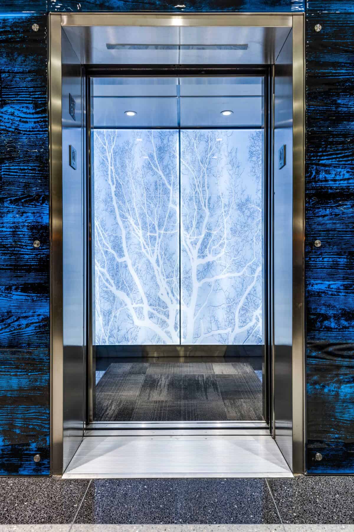 Michigan Lobby Remodel with Custom Blue Glass Wall and Back Lit Glass with Trees in the Elevator by Commercial Builder & General Contractor Structural Enterprises